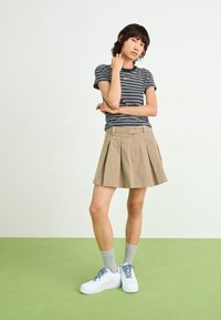 Striped black and white t-shirt, khaki pleated skirt, white sneakers with gray laces, and light gray ankle socks. Plain background and green floor.