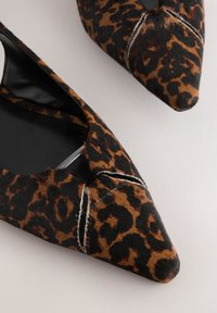 Scarpe basse con stampa leopardata e punta a punta, realizzate in materiale strutturato; presentano un design con ritagli e dettagli di cuciture bianche a contrasto.