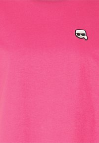 Różowa koszulka z krótkim rękawem wykonana z bawełny, z małą czarno-białą grafiką w okularach przeciwsłonecznych na lewej piersi.