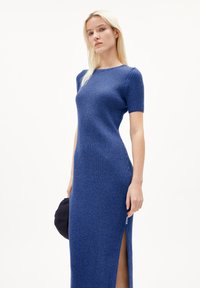 Blue ribbed knit dress with short sleeves, form-fitting silhouette, side slit, and subtle texture. Accompanied by a dark hat.
