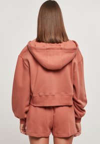 Tilbaketrukket hettegenser i dempet rosafarge, med en cropped design, myk tekstur og løse ermer kombinert med matchende shorts.
