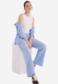 Camicetta a righe blu chiaro e pantaloni larghi abbinati, indossati con un top bianco e scarpe da ginnastica nere e bianche. Tessuto dalla consistenza liscia.