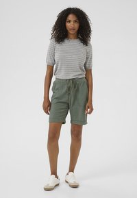 Chemise à rayures grises à manches courtes associée à un short en lin vert avec des poches latérales et une taille à cordon, complétée par des baskets blanches.
