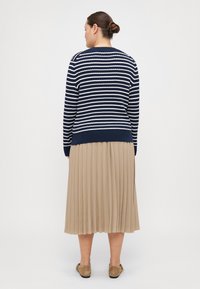 Navy and white striped knit sweater with round neck, paired with a beige pleated skirt. Soft texture, ankle-length, finished with flat shoes.