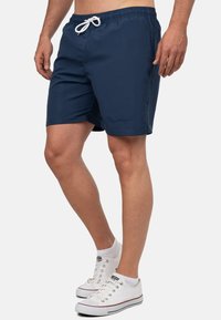 Marineblauwe zwemmers met een elastische tailleband en witte trekkoord. Gladde stof, knielang, met een subtiele logo-detail.