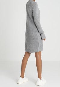 Robe pull en maille grise à manches longues et coupe décontractée, allant jusqu'à mi-thigh avec des poignets côtelés, assortie à des baskets blanches.