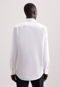 Camicia bianca a maniche lunghe con finitura testurizzata, dotata di un colletto classico, orlo arrotondato e dettagli con bottoni ai polsini.
