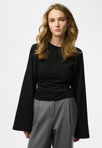 Top nero a maniche lunghe con maniche larghe, realizzato in tessuto morbido, abbinato a pantaloni grigi a righe sottili, caratterizzati da una vestibilità comoda e dettaglio in vita arricciata.