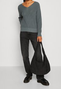 Szary dziergany sweter z dekoltem w serek i wzorem w jodełkę; połączony z czarnymi dżinsami i pikowaną czarną torebką na ramię; czarne buty.