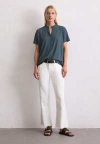 Türkises Kurzarmtop mit Stehkragen und Knopfleiste, kombiniert mit weißen ausgestellten Jeans und schwarzen flachen Sandalen. Schlichtes und lässiges Design.