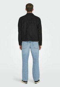 Svart mockajacka med krage, tillsammans med ljusblå denimjeans. Jackan har en �åtsittande passform och minimal hårdvara.