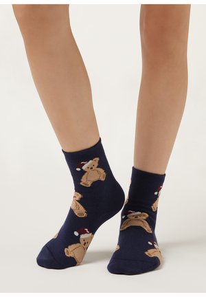 Calze blu navy con motivo orsetto, che indossano cappelli rossi e bianchi. Realizzate in tessuto morbido con polsino a costine per una vestibilità aderente.