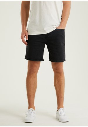 Shorts de mezclilla negra con corte recto, con un dobladillo deshilachado. Combinados con una camiseta de color claro y zapatillas blancas.