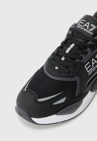 Zwarte sportieve schoen met een bovenwerk van mesh, synthetische accenten en een rubberen zool. Zilveren logo aan de zijkant en reflecterende details aanwezig.