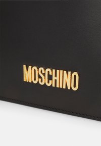 Svart läderväska med präglad guld "MOSCHINO"-logotyp, slät yta och rena linjer med synlig sömnad.