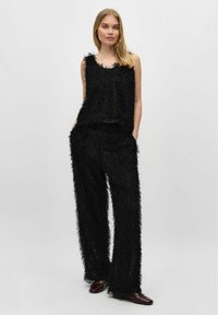 Zwarte textuuroutfit met een mouwloze top en losse broek met een franjesdesign. Het materiaal lijkt zacht en fuzzy.