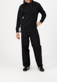 Czarna bluza z ribbowanymi mankietami, połączona z luźnymi czarnymi spodniami. Czarne sneakersy z białymi paskami. Jasnoniebieska torba na ramię.