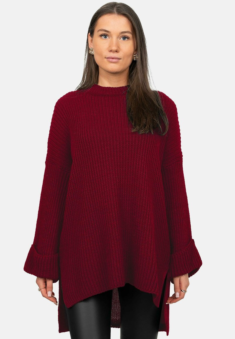 Pull en maille bordeaux avec texture côtelée, col montant et manches évasées. Dispose d'un ourlet arrière plus long et de fentes latérales pour une coupe décontractée.