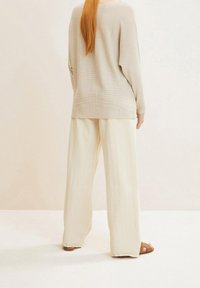 Beige Langarmoberteil mit gerippter Textur, kombiniert mit lockeren, cremefarbenen weiten Hosen. Einfaches Design mit hellen Sandalen.