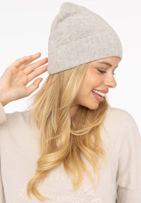 Light gray knitted beanie with a ribbed cuff, soft texture, and a peaked top. Worn by an individual with long, flowing hair.