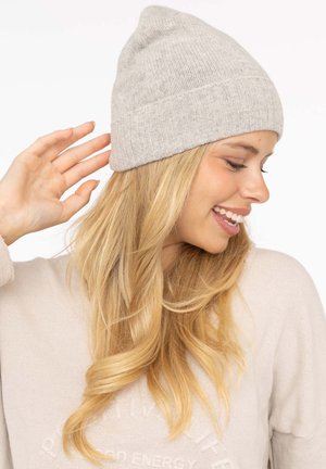 Light gray knitted beanie with a ribbed cuff, soft texture, and a peaked top. Worn by an individual with long, flowing hair.