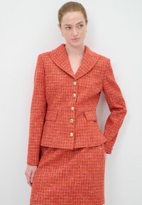 Roter Tweed-Anzug mit einer Peplum-Jacke, breitem Kragen, goldenen Knöpfen und einem passenden Rock mit texturiertem Finish und Fronttaschen.