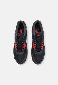Le sneakers Nike nere e rosse presentano una tomaia in mesh, suole in gomma, cuciture dettagliate e un logo swoosh bianco ben visibile sui lati.