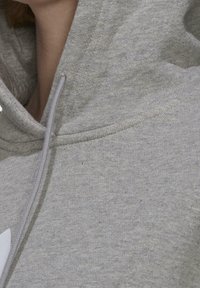 Grå hoodie i mjukt material. Har en dragkedja i huvan och en vit logotyp på framsidan. Slät yta med minimala inslag.