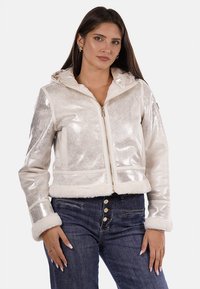 Giacca corta metallica bianca con rifiniture in pelliccia sintetica, chiusura zip frontale e cappuccio. Presenta quattro tasche e una superficie testurizzata per un tocco di dettaglio in più.