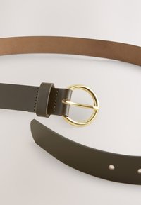 Pasek ze skóry w kolorze oliwkowej zieleni z okrągłą klamrą z metalu w odcieniu złota, charakteryzuj�ący się gładką fakturą oraz brązową spodnią stroną bez widocznych dziurek.