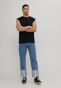 Camisa sin mangas negra, jeans azules con puños a rayas y zapatillas negras. Los jeans tienen un corte relajado y un diseño de puño distintivo.