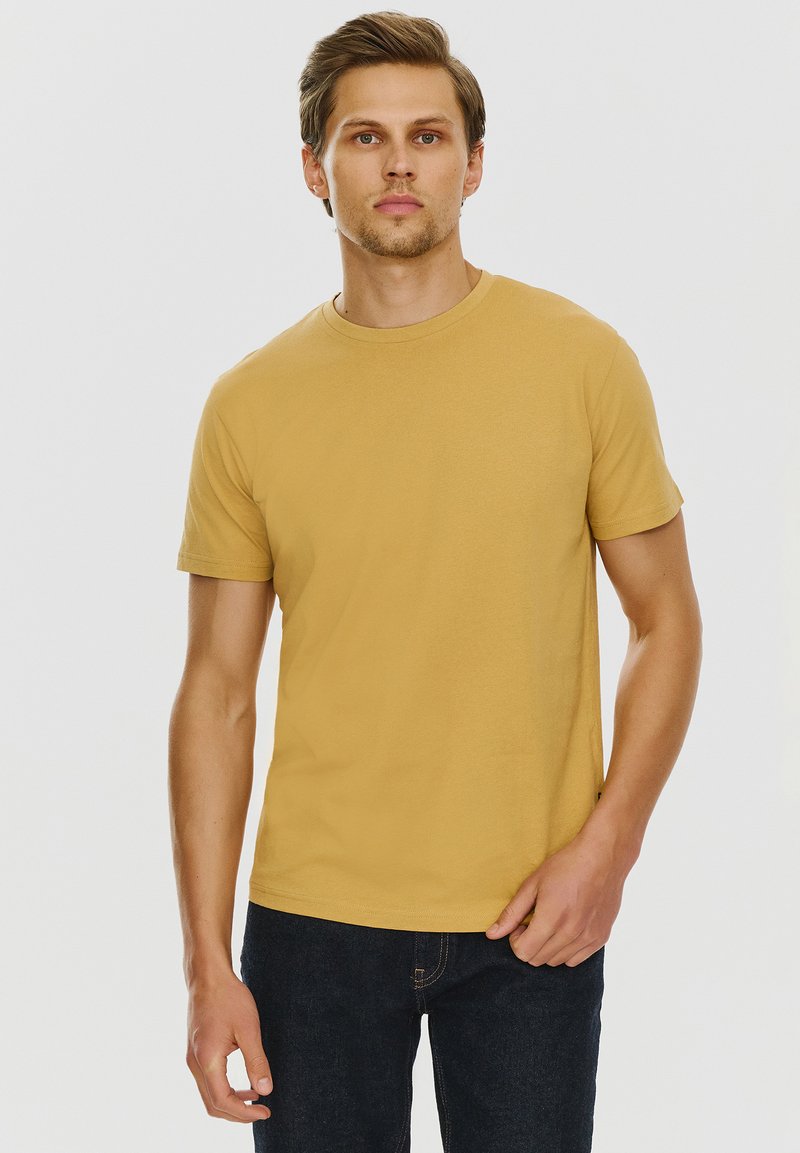 Żółta koszulka z krótkim rękawem, okrągły dekolt, wykonana z gładkiej bawełny, w zestawie z ciemnoniebieskimi dżinsami. Minimalistyczny design, bez widocznych wzorów.