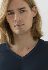 Granatowa koszulka typu v-neck, o miękkiej fakturze i dopasowanym kroju, z kontrastowym dekoltem w kształcie litery V oraz gładką tkaniną w zestawieniu z jasną skórą.