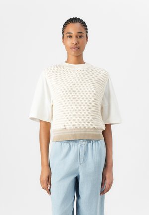 Maglione lavorato a maglia con parte superiore texturizzata color crema, maniche corte e orlo a coste beige, abbinato a pantaloni azzurri con cordino.