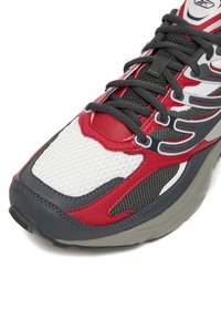 Roter und weißer Netzsneaker mit grauen Akzenten, strukturierten Überzügen und schwarzen Schnürsenkeln. Verfügt über eine gepolsterte Sohle und ein unterstützendes Design.