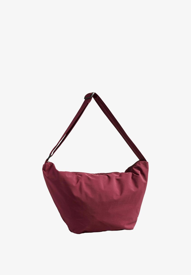 Bordeauxfarbene Tasche mit einem lässigen Design, weichem Stoff und einem einzigen verstellbaren Trageriemen für das Tragen über der Schulter oder als Umhängetasche.