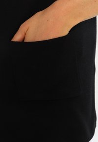 Black pullover with a side pocket. Soft, knit fabric with a smooth texture. Features a relaxed fit and clean edges.