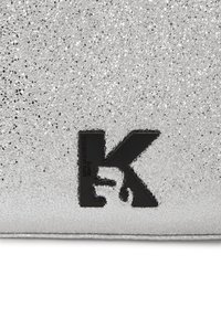 Ezüst csillámos klüts, texturált felülettel, fekete "K" logóval és sima fekete díszítéssel. Téglalap alakú, fémes fényű.