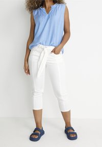 Light blue sleeveless top with a ruffled neckline, paired with white cropped pants and blue strappy sandals. Simple, casual outfit.