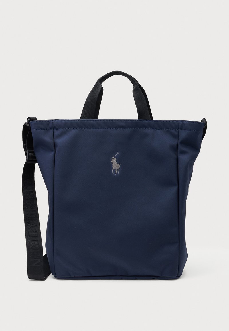 Sac fourre-tout bleu marine avec poignées noires et bandoulière réglable, arborant un petit logo joueur de polo argenté centré à l'avant.