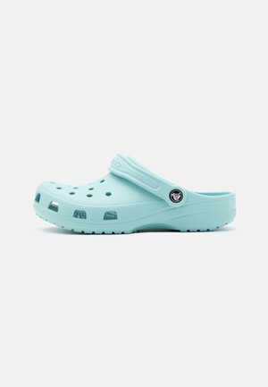 Hellblauer Clog-Schuh mit Belüftungslöchern, strukturierter Sohle und verstellbarem Fersenriemen mit rundem Logo auf weißem Hintergrund.