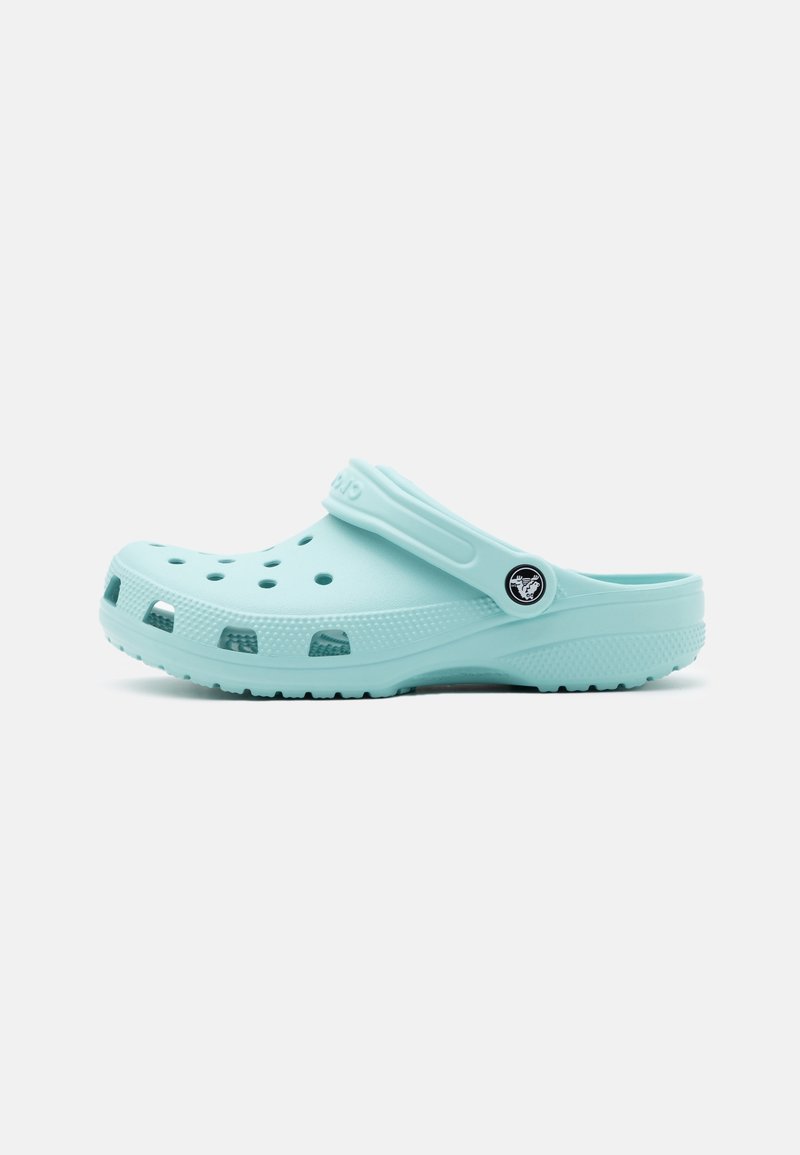 Sabot bleu clair avec trous de ventilation, semelle texturée et bride de talon réglable comportant un logo circulaire sur fond blanc.