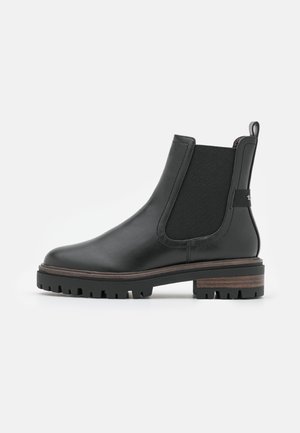 Botte Chelsea noire en cuir avec panneau latéral élastique, languette de traction au talon, semelle crantée et talon bas empilé sur fond blanc uni.