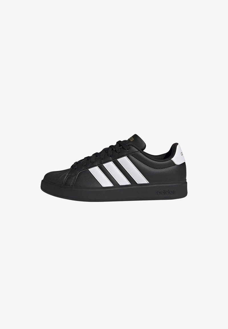 Baskets basses Adidas noires avec trois bandes blanches sur les côtés, lacets noirs et une languette blanche au talon.