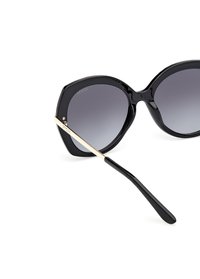 Gafas de sol negras de gran tamaño con lentes degradados de oscuro a claro, montura brillante y brazos metálicos con acentos dorados. Textura suave y forma audaz.