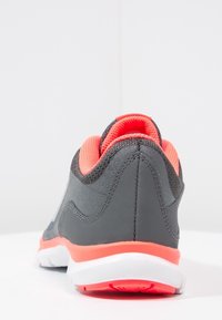 Urheilukenkä, jossa on harmaa synteettinen päällinen, oranssi verkkovuori, pyöristetty kärki ja valkoinen pohja oransseilla yksityiskohdilla.