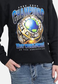 Sudadera negra con un diseño gráfico colorido que presenta un globo y un anillo de campeonato, mostrando el texto "Campeones" y "HUF WORLDWIDE".