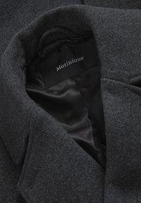 Grå ullkappa med ett slätt svart foder invändigt. Etiketter och sömmar synliga, med en klassisk krage och en strukturerad form.