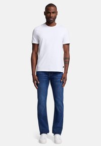 Biała koszulka z krótkim rękawem połączona z niebieskimi dżinsami i białymi trampkami. Koszulka ma okrągły dekolt i dopasowany krój.