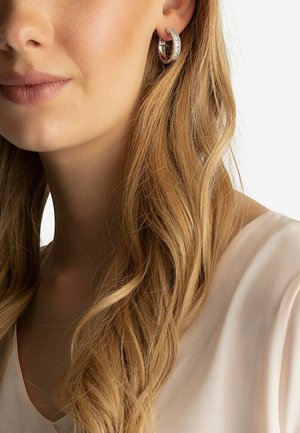 Zilveren hoepeloorbellen met een gestructureerd ontwerp en een rij heldere sprankelende accenten, gedragen door een model met lang golvend haar.